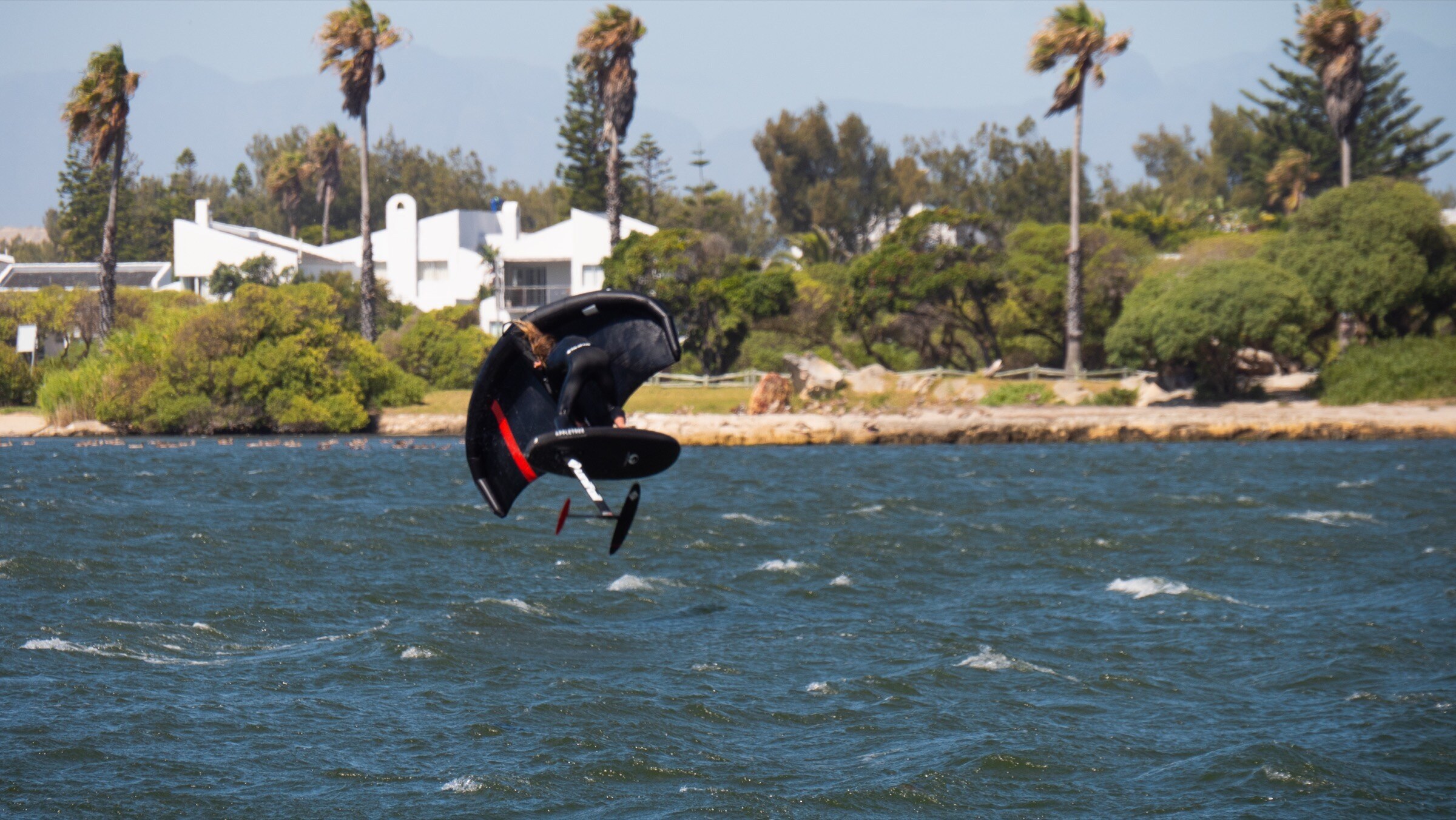 Kitesurf foiling action over turquoise water.