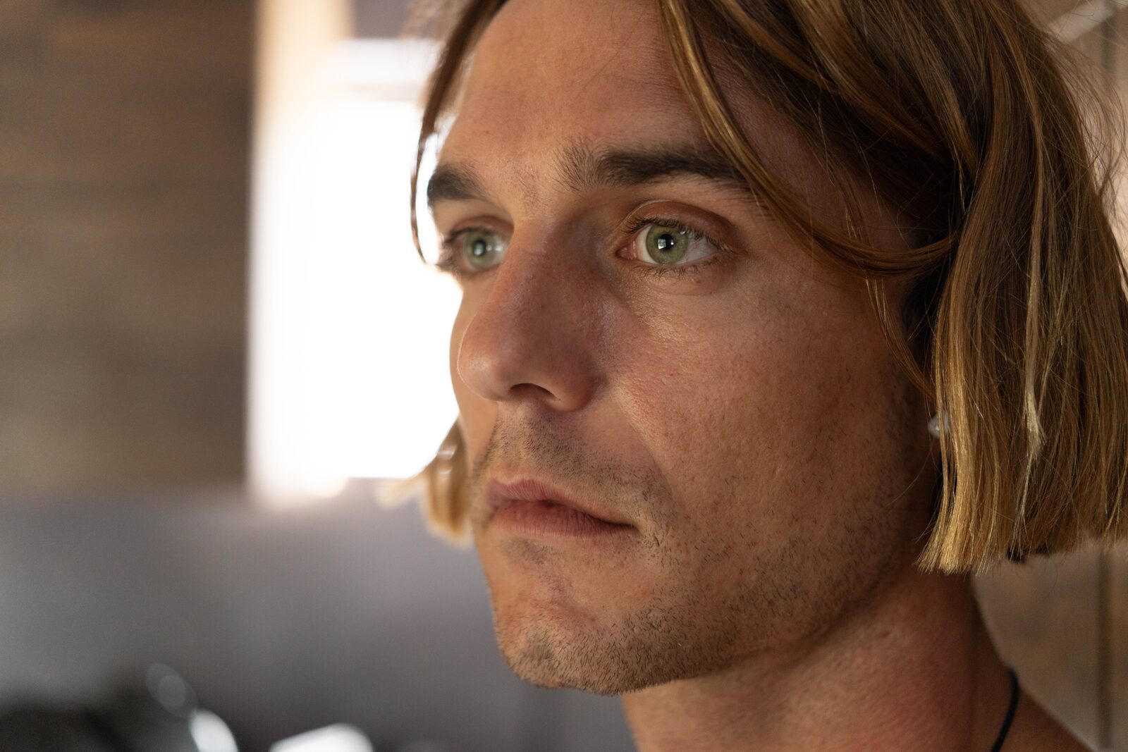 Side-lit editorial portrait of Dylan Wichmann looking off-camera in warm window light.